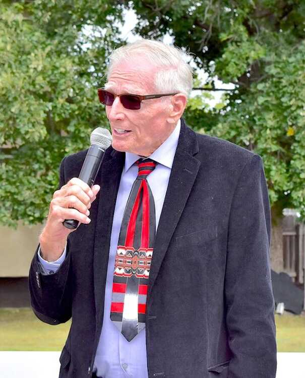 Allen Strunk (BSJ51) speaking into a microphone, wearing a suit and patterned tie.