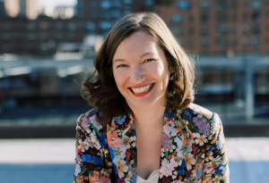 A woman in a flower-patterned blazer smiles at the camera.